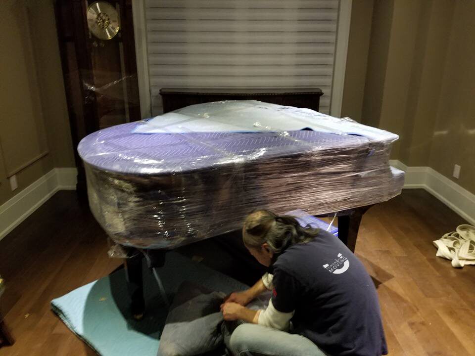 Billy from Toronto movers packing a grand piano with protective padding and plastic wrap.