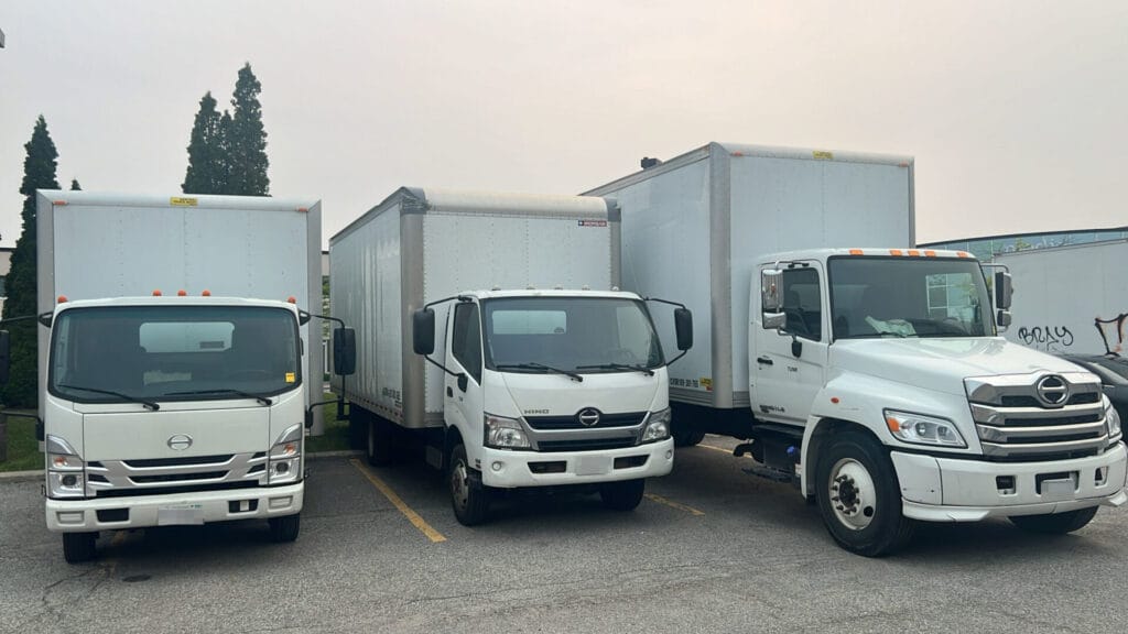 Front view of three white moving trucks of different sizes parked in a row at Toronto Unique Moving