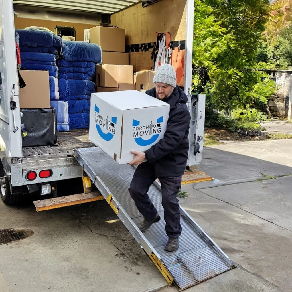 Mover in a white beanie loading a branded Toronto Unique Moving box into a truck using a ramp.