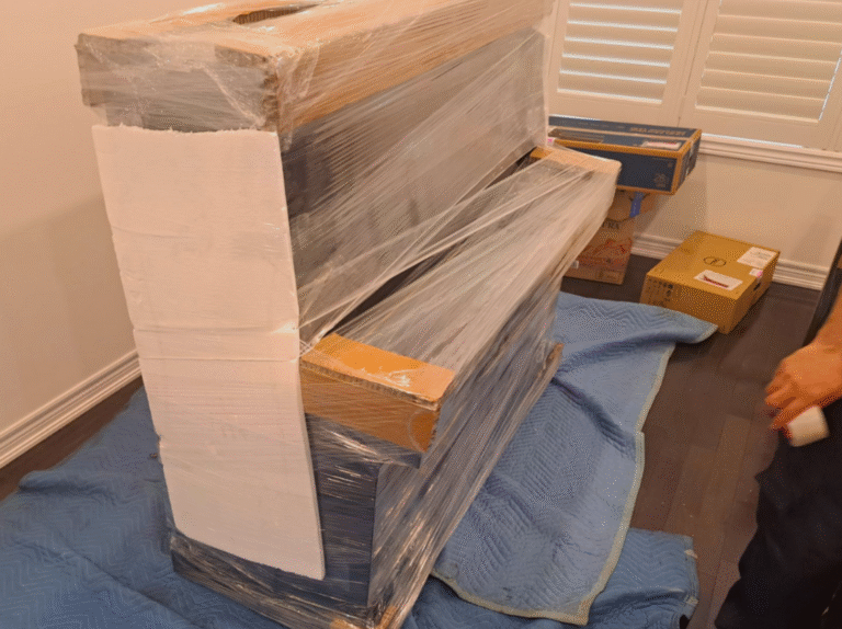 Upright piano on moving blankets with corner guards and plastic wrap applied by professional packers in Toronto.