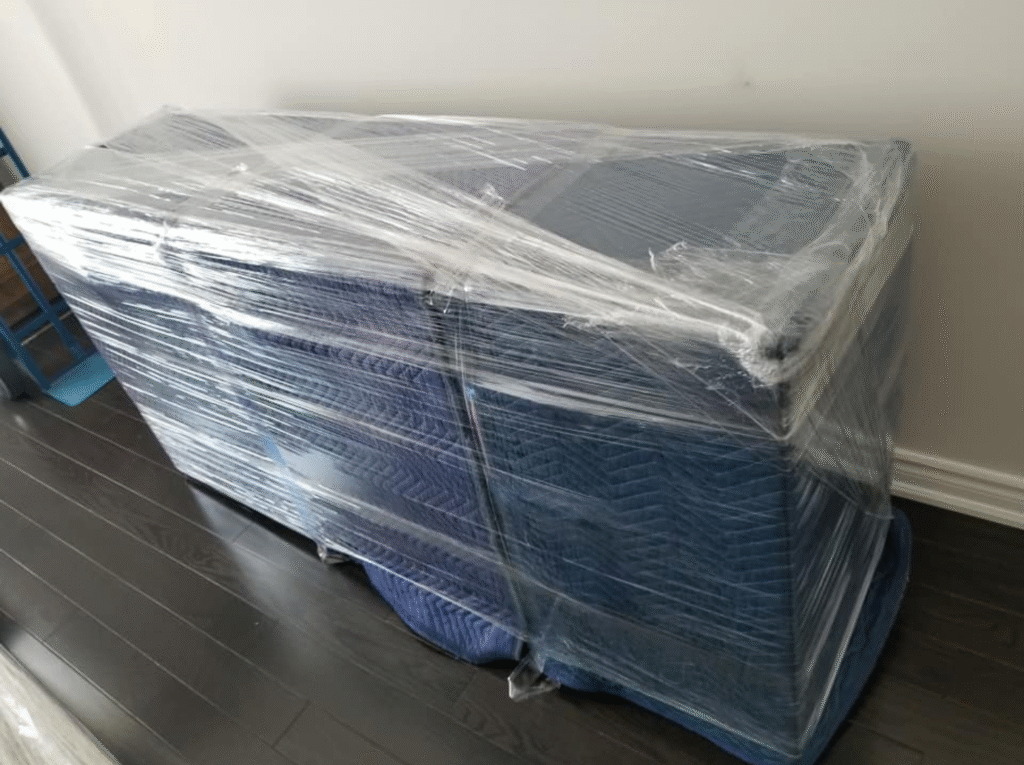 Wrapped wooden dresser secured with moving blankets and stretch wrap for safe transport in Toronto.