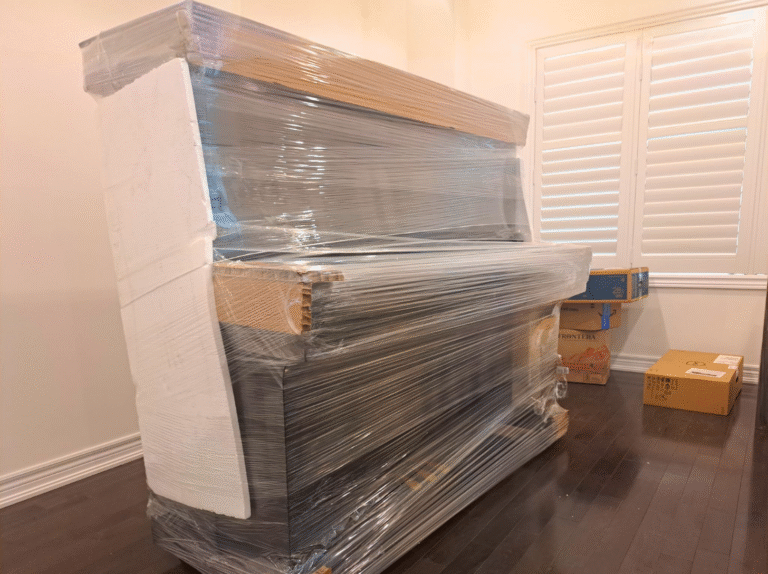 Upright piano fully wrapped with foam boards and stretch film by Toronto piano movers for safe transport.