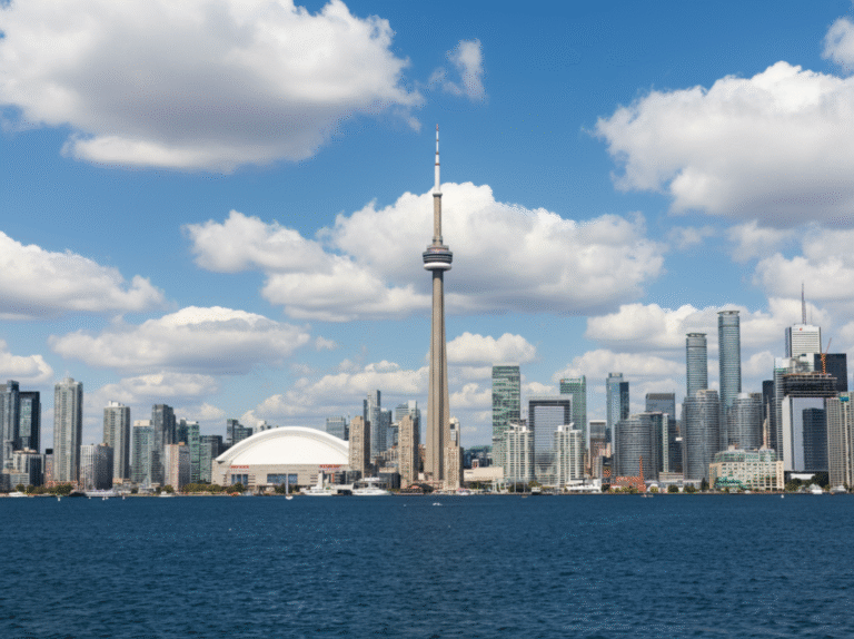 CN Tower centered above Toronto’s waterfront skyline with Rogers Centre and condos under scattered clouds.