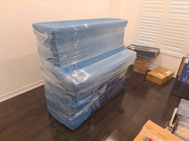 Upright piano fully covered with blue moving blankets and stretch wrap, ready for transport in Toronto.
